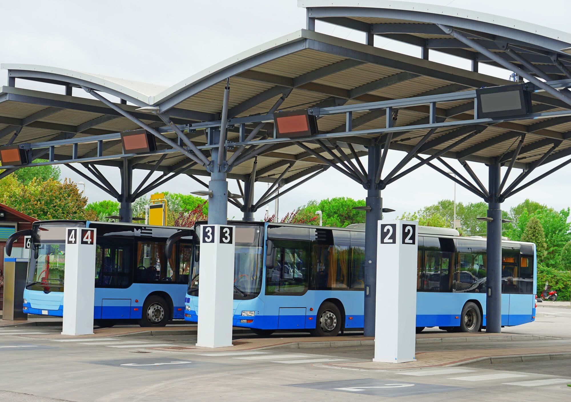 Three blue transit buses line up under a shelter at a transit hub.
