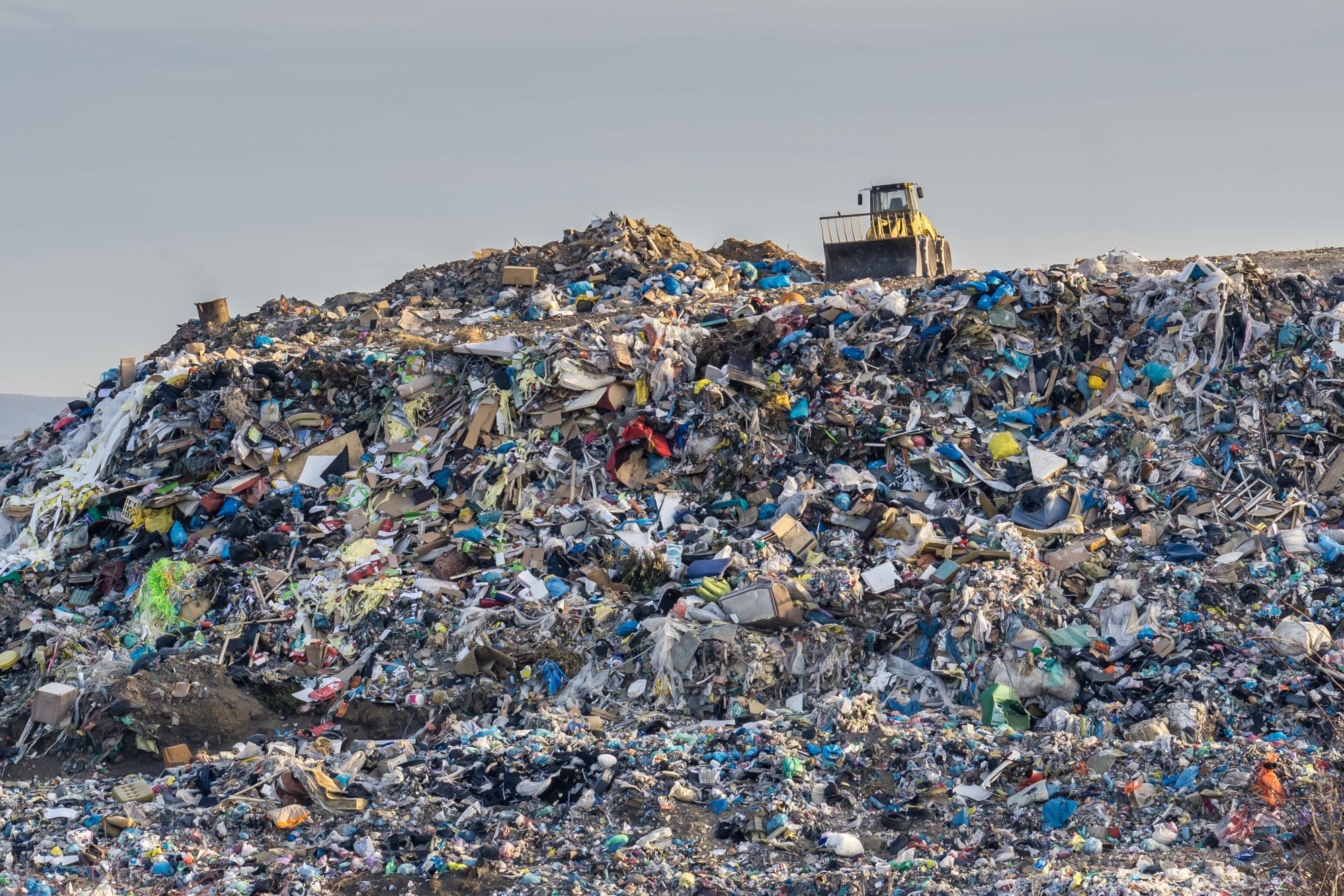 A dozer travels across the surface of a large landfill site over mixed waste and debris.